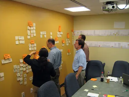 grouped similar tasks on office wall during team meeting with color-coded sticky note clusters and collaborative discussion