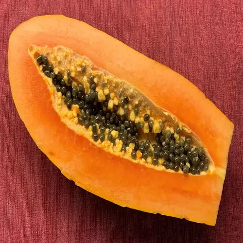 halved ripe papaya fruit with orange flesh and black seeds on red textured background