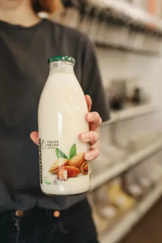 hand holding a glass almond milk bottle (volko molko brand) with almond graphics, against a store shelf background