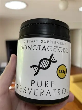 hand holding black resveratrol supplement powder container (183g) from donotage.org, featuring dna double helix graphic and bold 'pure resveratrol' text label