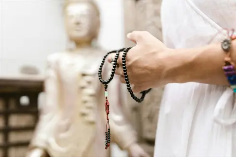 hand holding meditation beads in front of a buddha statue, embodying mantra simplicity