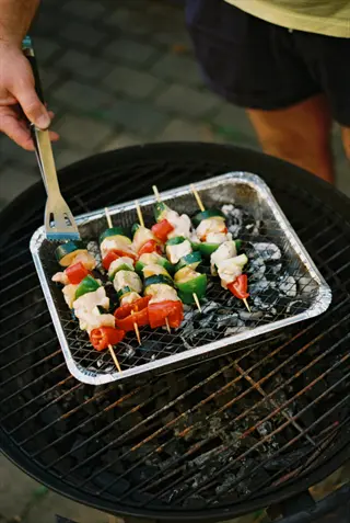 hand using tongs to grill vegetables skewers (mixed with meat) on a charcoal grill outdoors