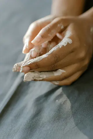 hands covered in white clay sculpting material on a gray fabric surface, demonstrating sensory engagement through tactile artistic creation
