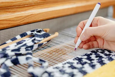 hands operating a wooden loom with striped fabric scraps and vibrant woven textile, embodying textile art through meticulous craft