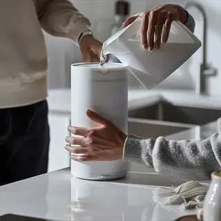 hands pouring water from a pitcher into a white water filter pitcher on a modern kitchen counter