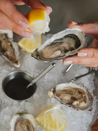 hands serving fresh oysters on ice with lemon wedges and sauce