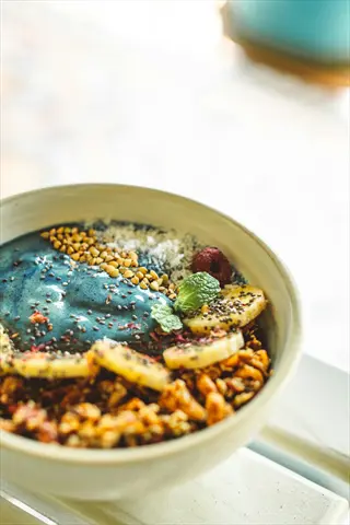healthy breakfast bowl featuring blue spirulina base, banana slices, chia seeds, granola clusters, coconut flakes, and fresh mint garnish on a bright table