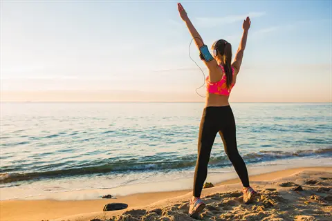 healthy morning outdoors: woman stretching on beach at sunrise with arms raised towards ocean, promoting immune system support through exercise