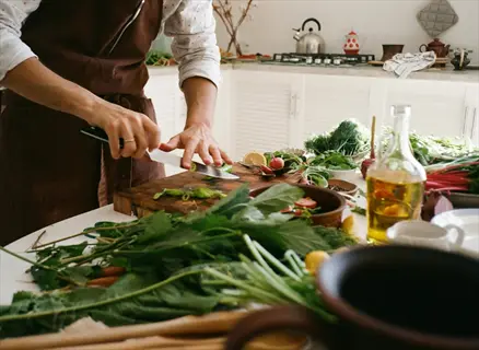home cooking vegetables: person chopping fresh greens on a cutting board in a kitchen, demonstrating cooking techniques with vegetables and kitchen tools
