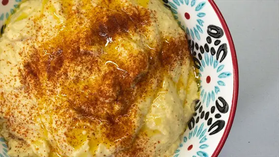 homemade hummus bowl topped with paprika and olive oil in a decorative patterned bowl