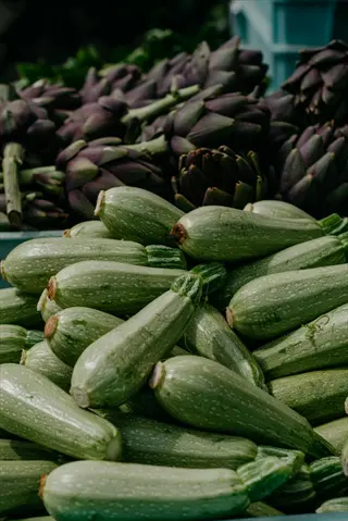 hydration fresh zucchini: pile of light green speckled zucchini with fresh artichokes at a market stand