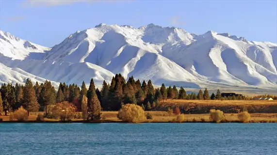 iconic new zealand landscape with snow-capped southern alps, turquoise glacial lake, and vibrant autumn forests under clear blue skies