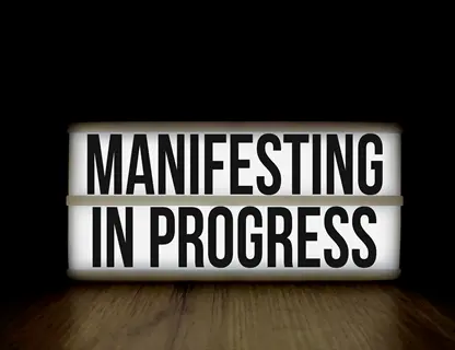 illuminated lightbox displaying 'manifesting in progress' text on dark background for vision board progress tracking