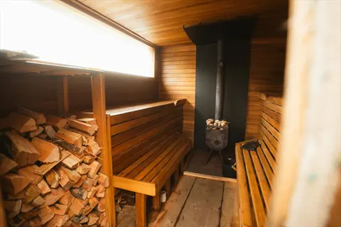 interior of a traditional wood-burning sauna with stacked firewood, wooden benches, and a stone heater