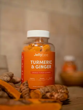 jellybee turmeric & ginger gummies bottle (turmeric joint health supplement) with fresh turmeric roots on rustic kitchen counter
