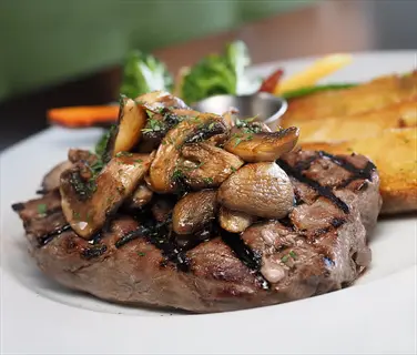 juicy beef steak with sautéed mushrooms, roasted potatoes and fresh vegetables on white plate
