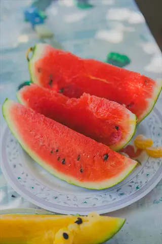 juicy watermelon pieces on a patterned plate outdoors with other fruits on a table