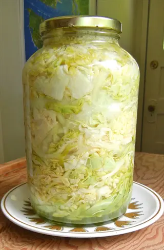large glass jar filled with homemade sauerkraut on decorative plate, wooden table surface, blurred background