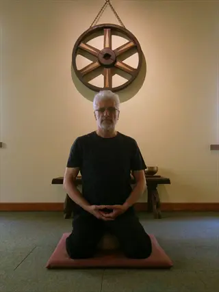 man performing seiza meditation kneeling on cushion in serene room with dharma wheel wall art