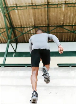 man performing stair sprints exercise on concrete stairs in outdoor stadium setting