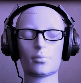 mannequin head wearing black and silver over-ear binaural beats headphones with black frame glasses, against light purple textured background
