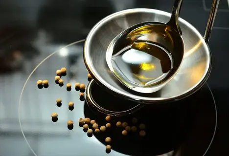 metal spoon with golden oil resting on stovetop, surrounded by scattered black seed oil seeds in morning light