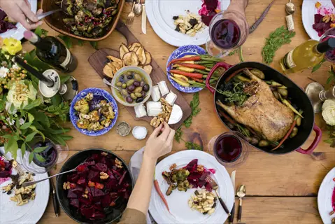 mindful eating: overhead view of rustic wooden table filled with colorful dishes, hands serving/eating, embodying mealtime awareness in a communal feast