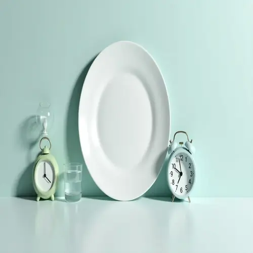 minimalist still life: two alarm clocks (intermittent fasting clocks), hourglass, water glass, and empty plate on a pastel green table