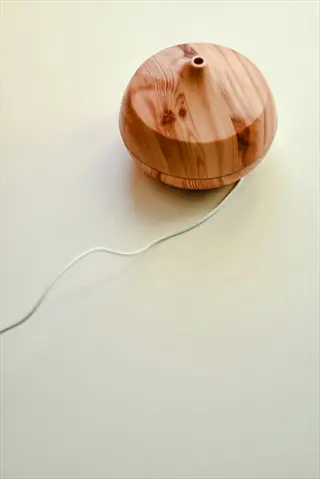 minimalist wooden essential oil diffuser with power cord on plain beige background for calming scents