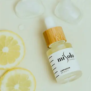 misolo essential oil lemon bottle (biphasic cleanser) with wooden dropper cap, surrounded by fresh lemon slices and ice cubes on a light beige surface