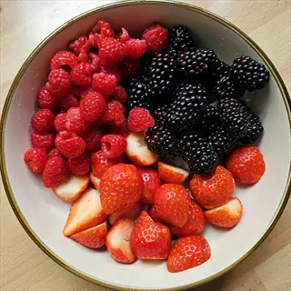 mixed berries bowl featuring strawberries, raspberries, and blackberries in a ceramic dish on a wooden surface