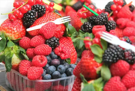 mixed fresh berries including strawberries, raspberries, blackberries, blueberries, and red currants piled in containers with plastic forks