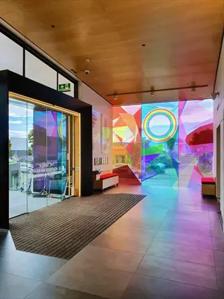 modern art gallery entrance with rainbow-hued geometric glass installations, embodying a safe art space through inclusive architecture and trauma-informed design