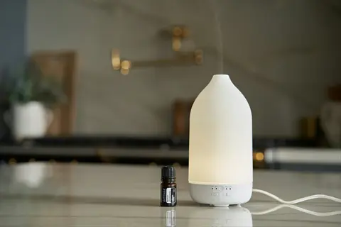 modern essential oil diffuser emitting mist next to oil bottle on kitchen countertop
