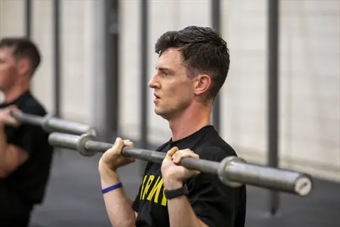 mountain athlete training: military soldier performing barbell shoulder press in gym, demonstrating strength and endurance for high-altitude operations, with fellow trainee visible in background