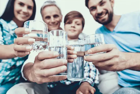 multi-generational family members (adults and child) holding water glasses together, demonstrating hydration for age groups