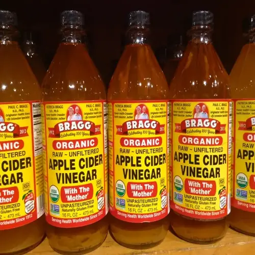 multiple bragg organic apple cider vinegar bottles with labels showing 'with the mother' and certifications on store shelf