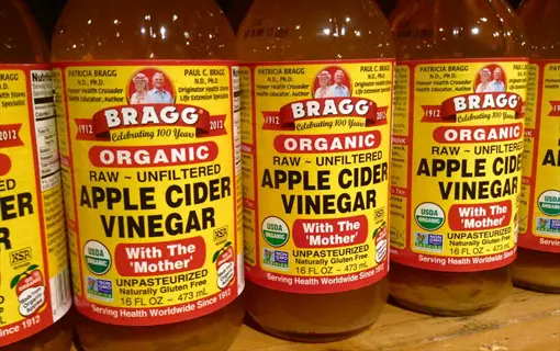 multiple bragg organic apple cider vinegar bottles with 'with the mother' labels on store shelf display