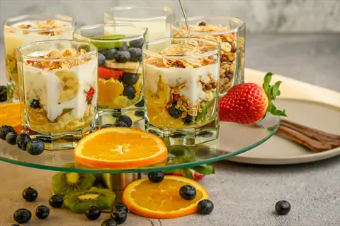 multiple layered yogurt parfaits in glasses with fresh strawberries, blueberries, oranges, and granola on display stand - calcium-containing foods
