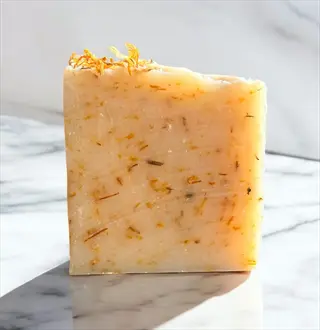 natural eczema herbal treatment soap bar with visible dried orange calendula flowers on marble surface