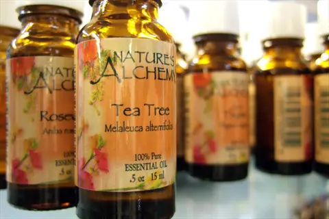 nature's alchemy tea tree essential oil bottle (melaleuca alternifolia) with floral label design, among other amber essential oil bottles on a shelf