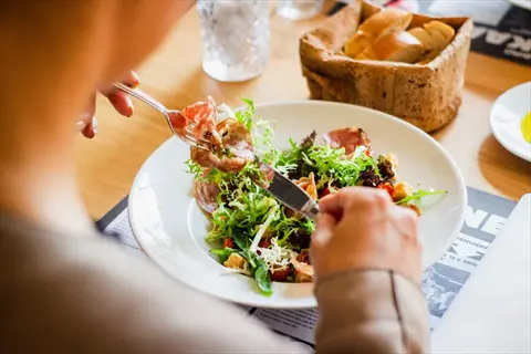 no distractions eating: person focused on a fresh salad using cutlery at a restaurant table, ignoring background text and side items (bread basket, water glass)