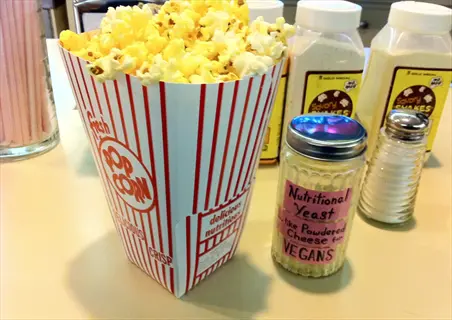 nutritional yeast popcorn in striped container with seasoning shakers on table