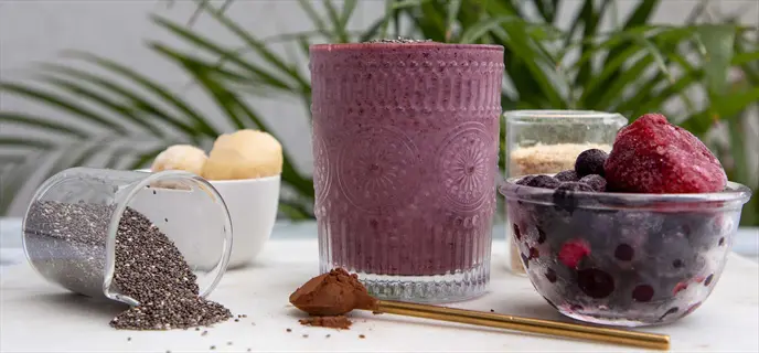 nutritional yeast smoothie in embossed glass with chia seeds, frozen fruit mix, and nutritional yeast powder as smoothie booster ingredients on marble surface
