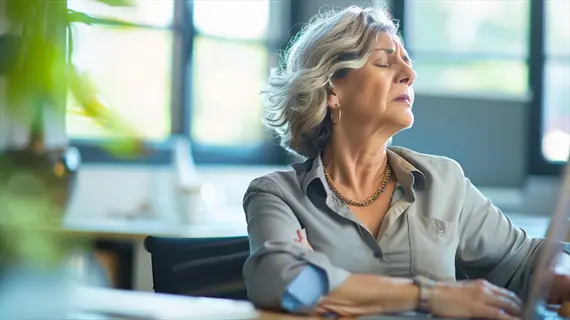 office desk breathing: woman practicing mindful breath at workstation in bright office space with potted plants, large windows, and natural light