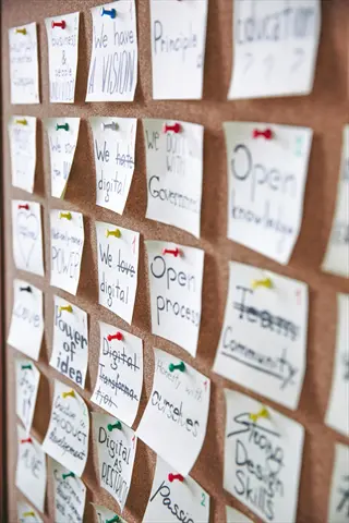 office vision board with colorful sticky notes pinned to corkboard, featuring handwritten messages about team goals, digital transformation, and creative motivation