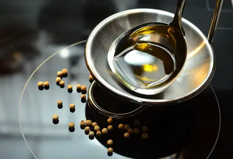 olive oil measured in a tablespoon, with peppercorns scattered on a dark surface