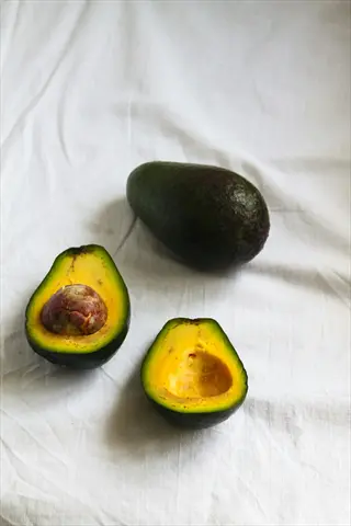 one whole ripe avocado and two ripe avocados halved (one with pit, one pitted) on a white cloth background