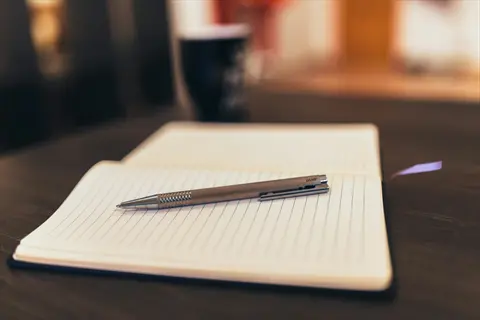 open lined notebook with pen resting on pages on wooden table, blurred background with warm lighting, embodying phase 3 consolidation