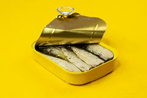 opened can of sardines canned in oil with pull-tab, on yellow background